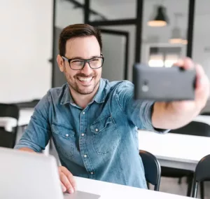 man in denim shirt smiling recording himself on phone